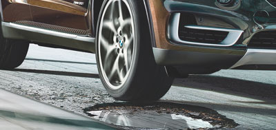BMW vehicle driving over a pothole in the road